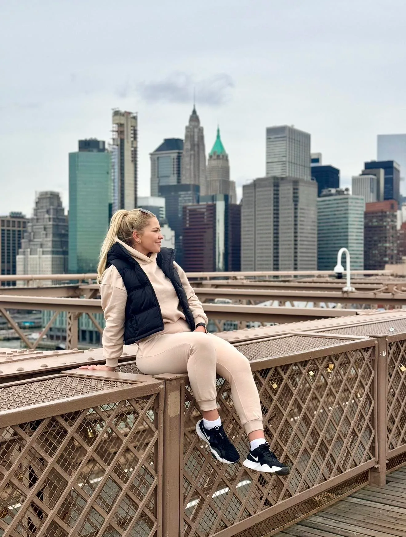 Nikol sedí na zábradlí Brooklynského mostu, za ní mrakodrapy Manhattanu